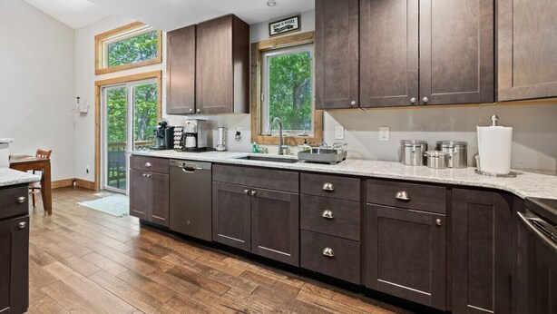 A modern kitchen with dark wood cabinets, a large island with a sink, and a view of the outdoors through the windows. - Silver Linings - Hot Tub, Mountain Views, Close to Town, Pet Friendly (Waynesville)