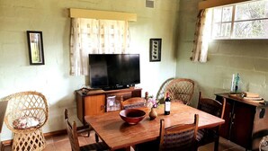 Un coin repas comprenant une table en bois, des chaises, un téléviseur et une fenêtre avec des rideaux.