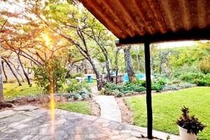 A covered patio area with stone flooring, surrounded by lush greenery and trees. - Remarkable 3-bed Cottage in Nyanga (Juliasdale)