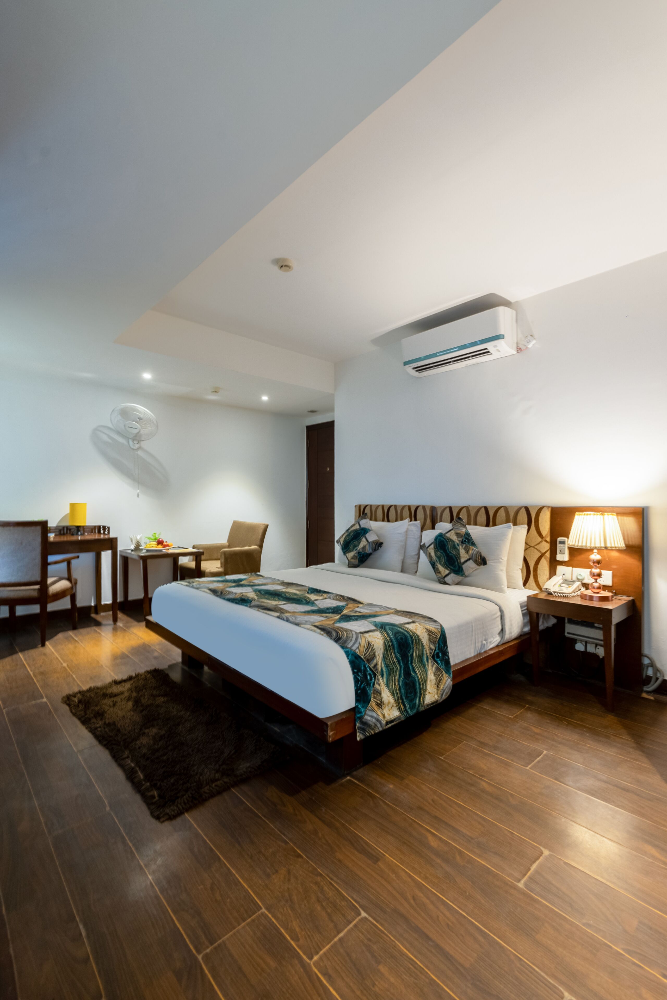 A modern hotel room with a large bed, a desk, a chair, and a small table.