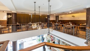 A multi-level restaurant with a modern design, featuring a central chandelier, wooden accents, and a view of the lower level. - Arch Plaza - Near Yashobhoomi Convention Centre Dwarka (New Delhi)