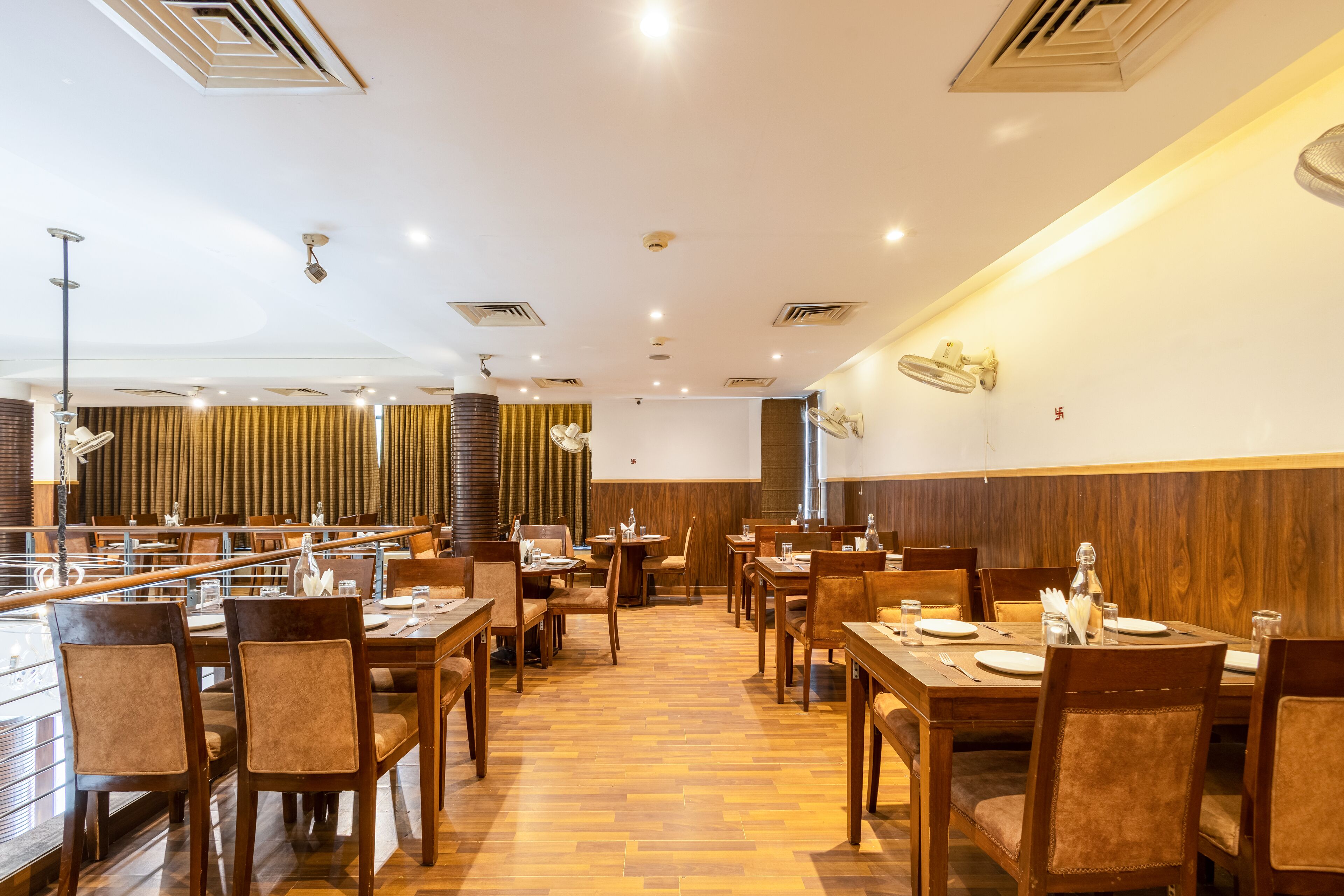 Een ruim restaurant met houten vloeren, meerdere tafels en stoelen, en een modern plafondontwerp.