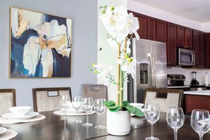 A dining table with white plates, glasses, and a potted orchid.