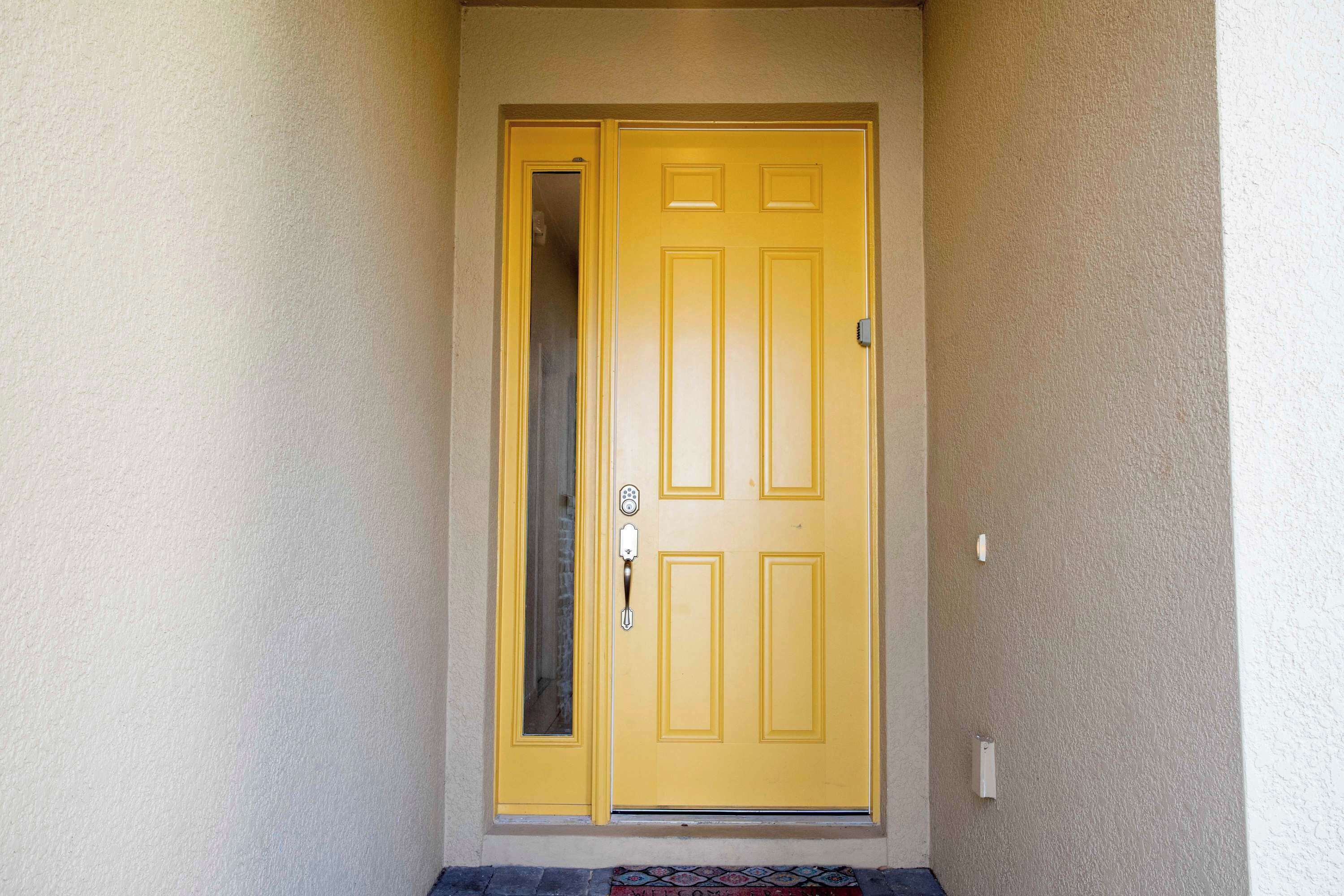 A yellow door with a glass panel and a doorbell.