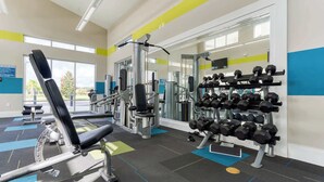 Un gimnasio con equipo de ejercicio, incluyendo una banca, máquinas de pesas y un estante con mancuernas.