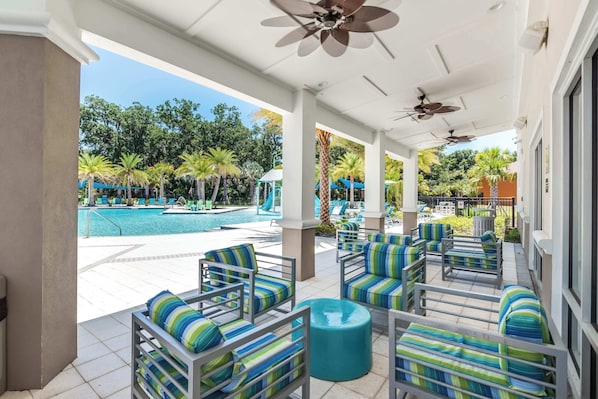 A covered outdoor seating area with striped chairs and a pool in the background.