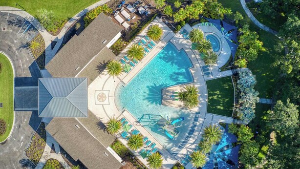 Vista aérea de un complejo turístico con una piscina central, varias zonas de descanso y abundante vegetación.