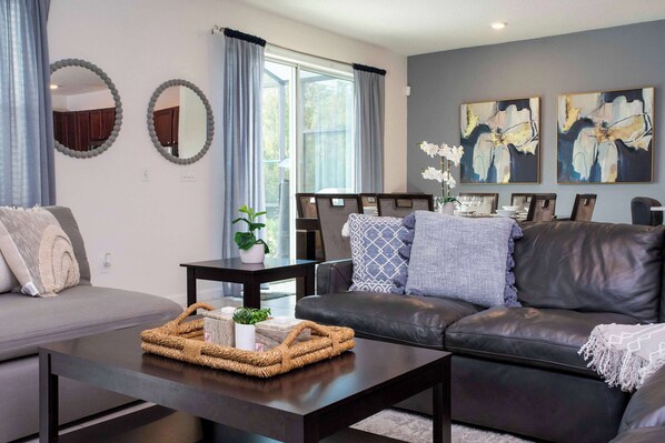 A modern living room with a dark leather sofa, a coffee table with a woven basket, and two round mirrors on the wall.