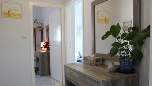 Un couloir avec une coiffeuse en bois, un miroir et une plante en pot.