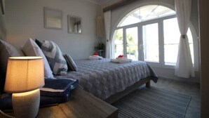 Une chambre à coucher avec un lit, des tables de chevet, une lampe et une grande fenêtre avec des rideaux.