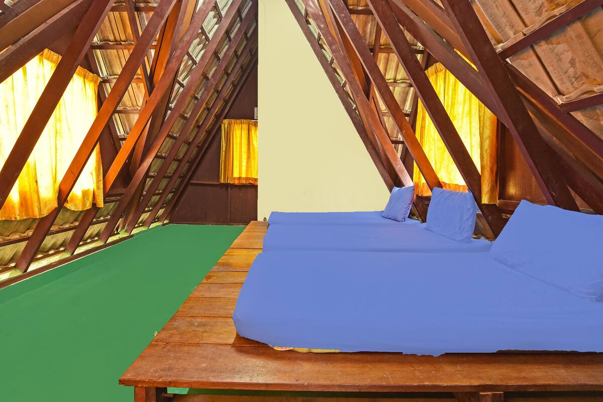 Una cama individual con colchón y almohadas azules en una habitación con techo inclinado y vigas de madera.