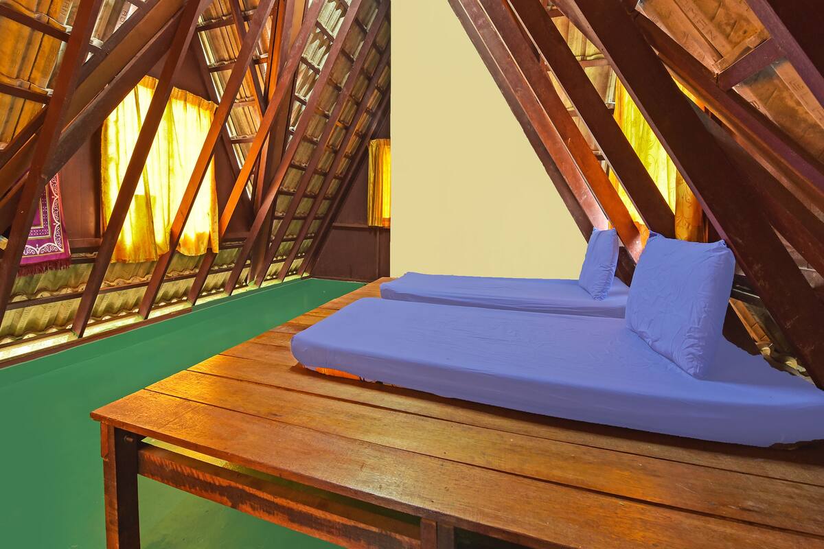Una cama de madera con colchón y almohadas en una habitación con techo inclinado y vigas de madera.