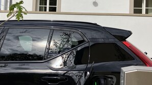 Een zwarte SUV geparkeerd voor een gebouw, met een oplaadpunt ervoor.