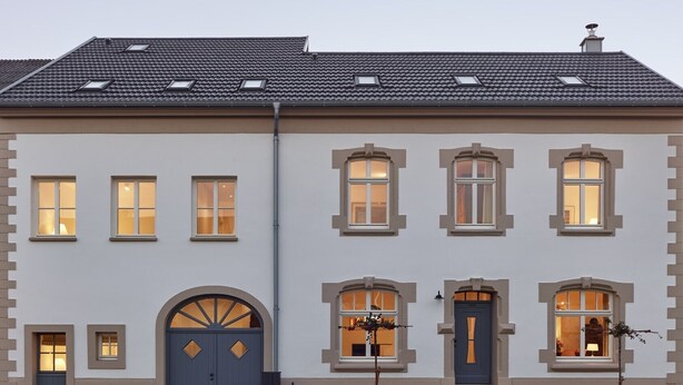 Een gebouw met twee verdiepingen en een symmetrische gevel, met een centrale ingang met een blauwe deur, aan weerszijden omringd door twee ramen.