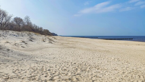A sandy beach with footprints, a clear sky, and a distant view of the ocean. - Cozy apartment in Lukecin with WiFi (Lukecin)