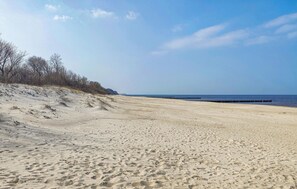 Ein sandiger Strand mit Fußabdrücken, einem klaren Himmel und einem fernen Blick auf das Meer.