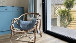 A wicker chair with a cushion in a room with a large window, a blue cabinet, and a view of a garden. - Charming house in the port of Sainte-Marine (Combrit)