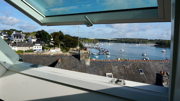 A view from a window overlooking a harbor with boats, a stone wall, and buildings in the background. - Charming house in the port of Sainte-Marine (Combrit)