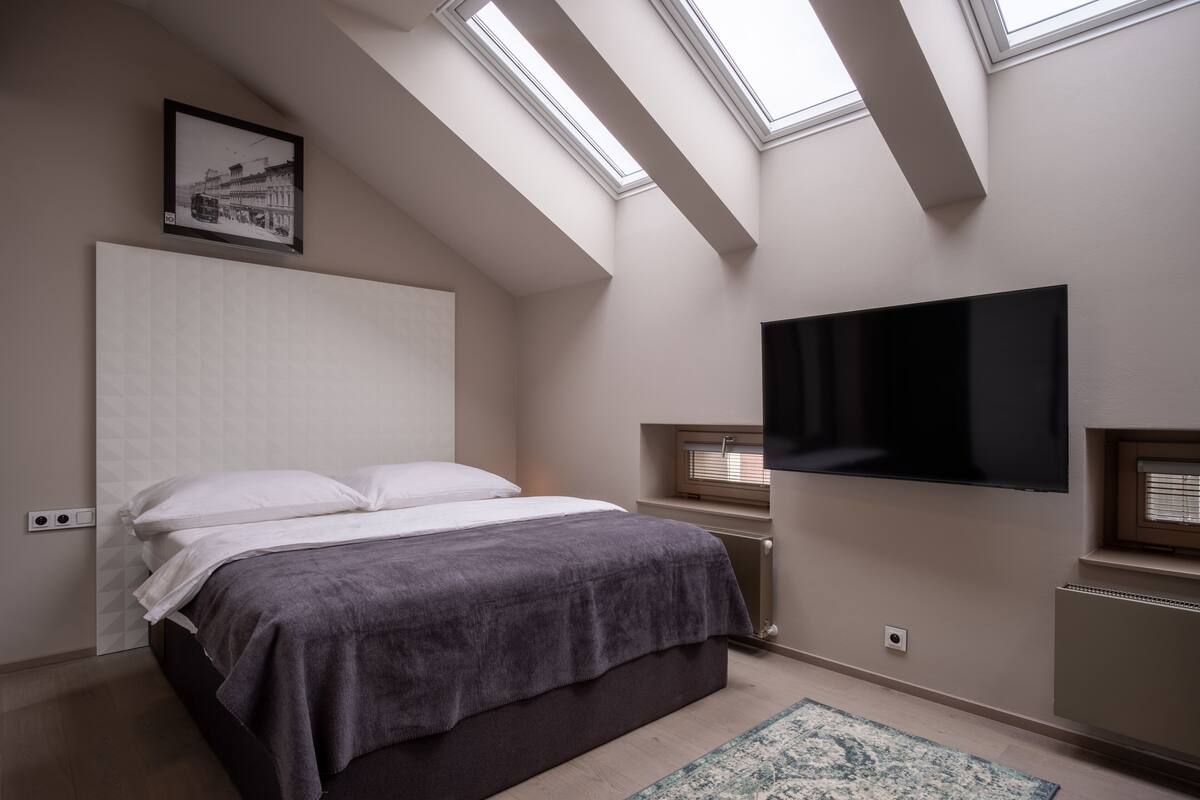 A bedroom with a bed, a TV mounted on the wall, and skylights.