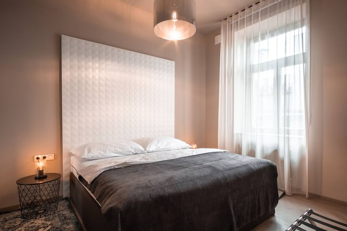 A modern bedroom with a large bed, a bedside lamp, and a window with sheer curtains.