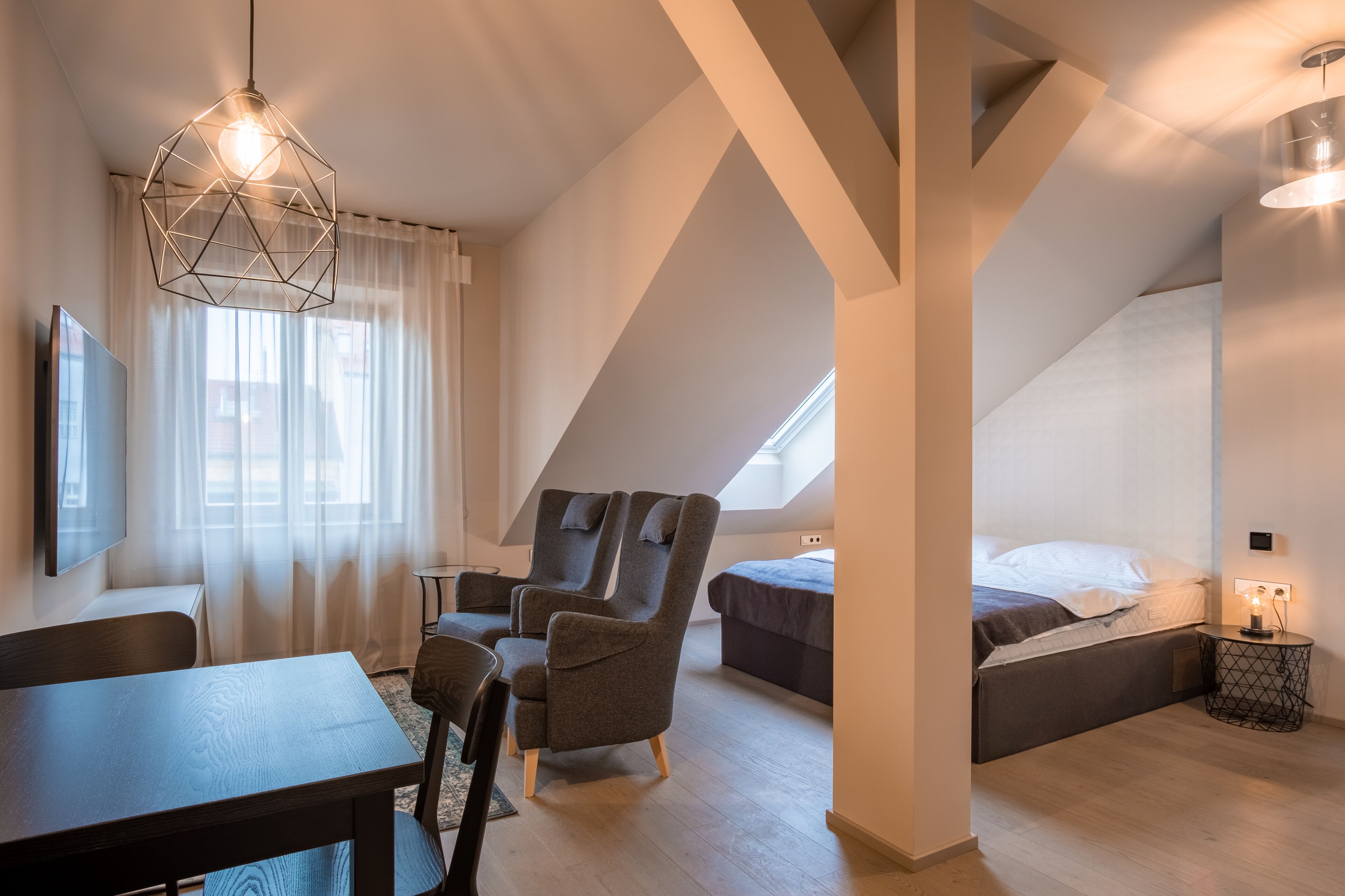 A modern loft bedroom with a sloped ceiling, a large window, a bed, a desk, and a chair.
