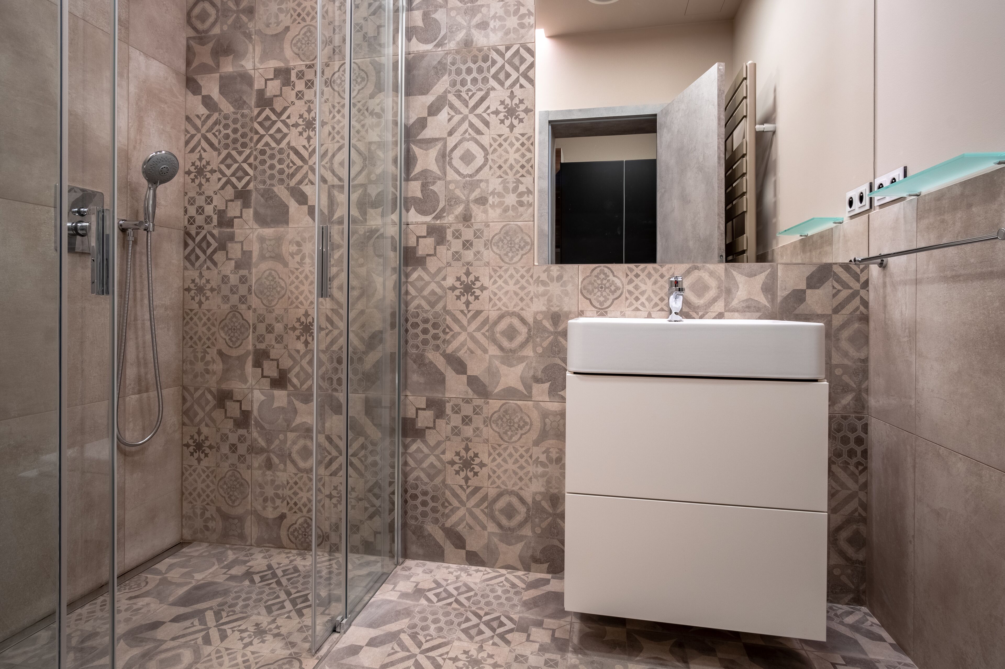 A modern bathroom with patterned tiles, a glass shower enclosure, and a white vanity.