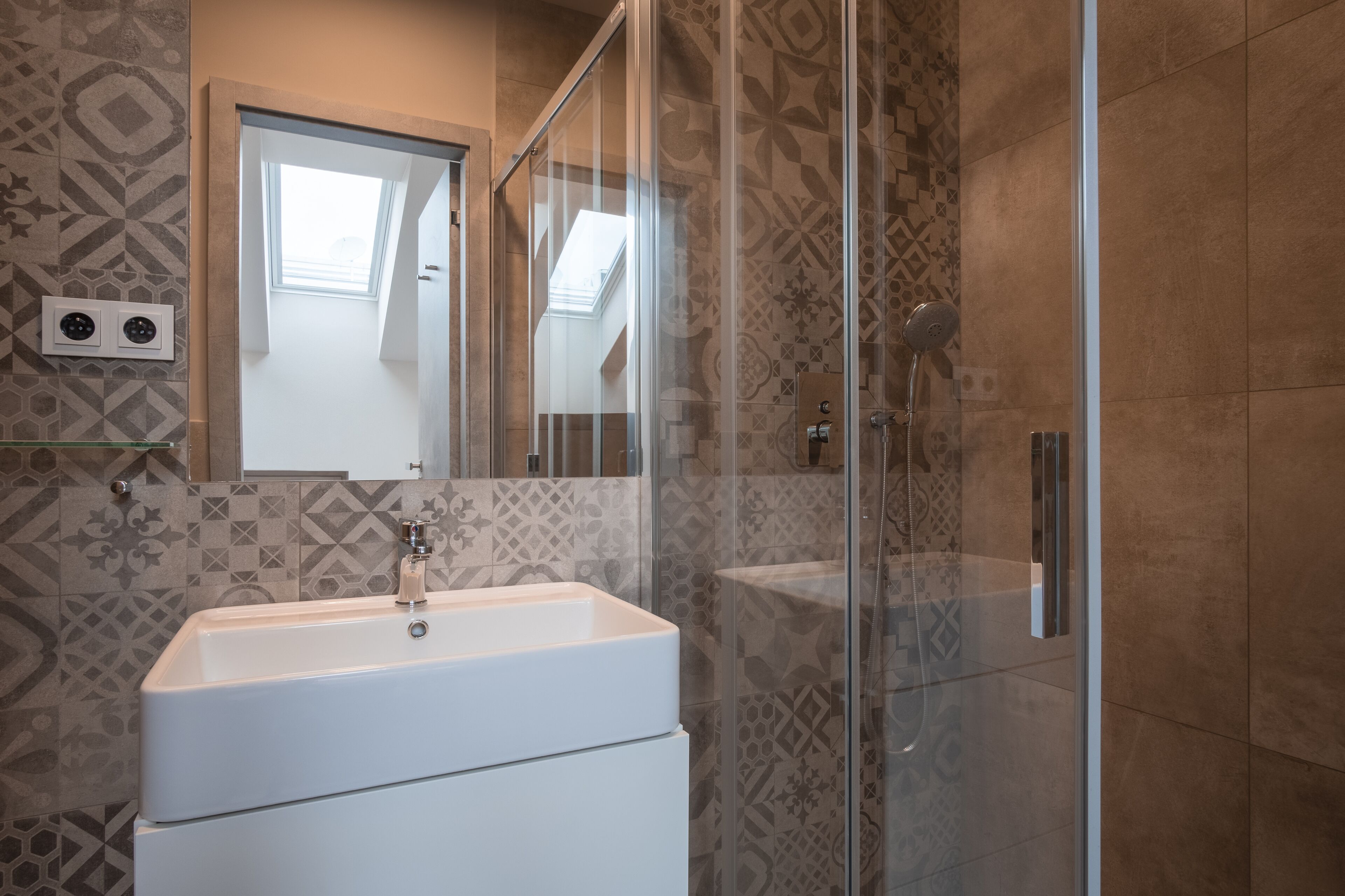 Ein modernes Badezimmer mit Duschkabine aus Glas, einem weißen Waschbecken und fliesenmuster.