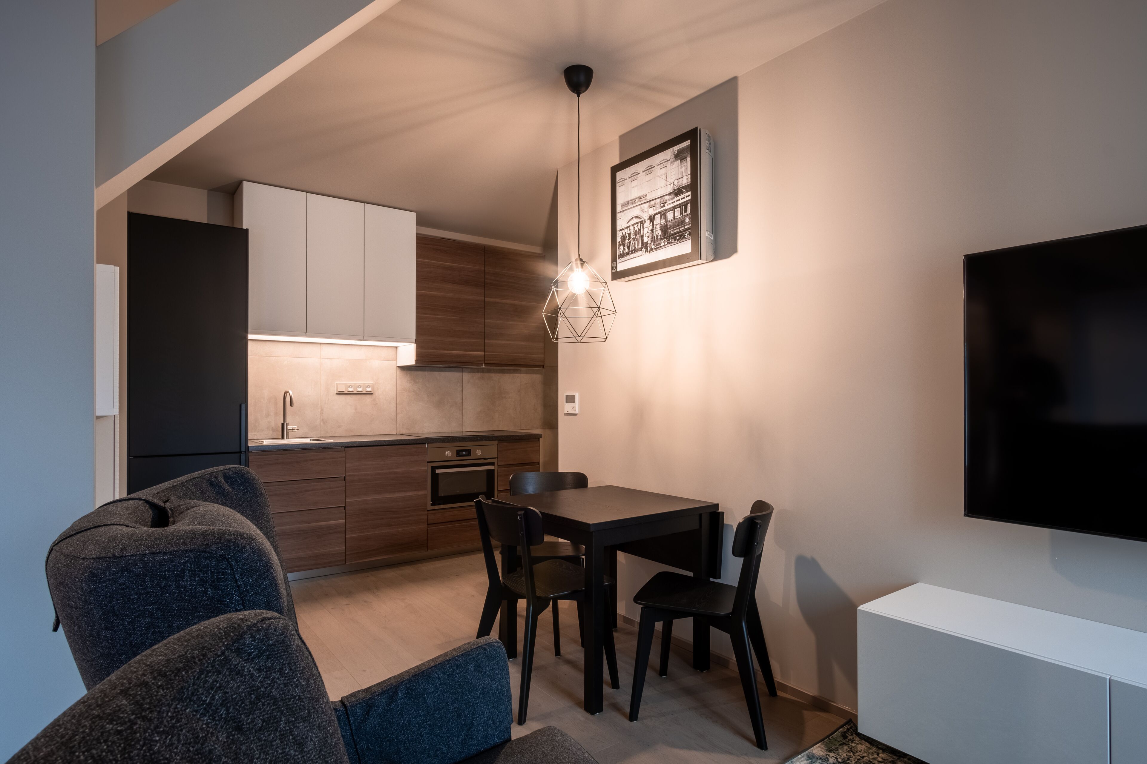 Una cocina moderna con armarios de madera, un comedor con mesa y sillas, y un televisor de pantalla plana montado en la pared.