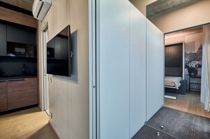 Una camera d'hotel moderna con angolo cottura, TV a schermo piatto montata a parete e un letto con vista sulla città.