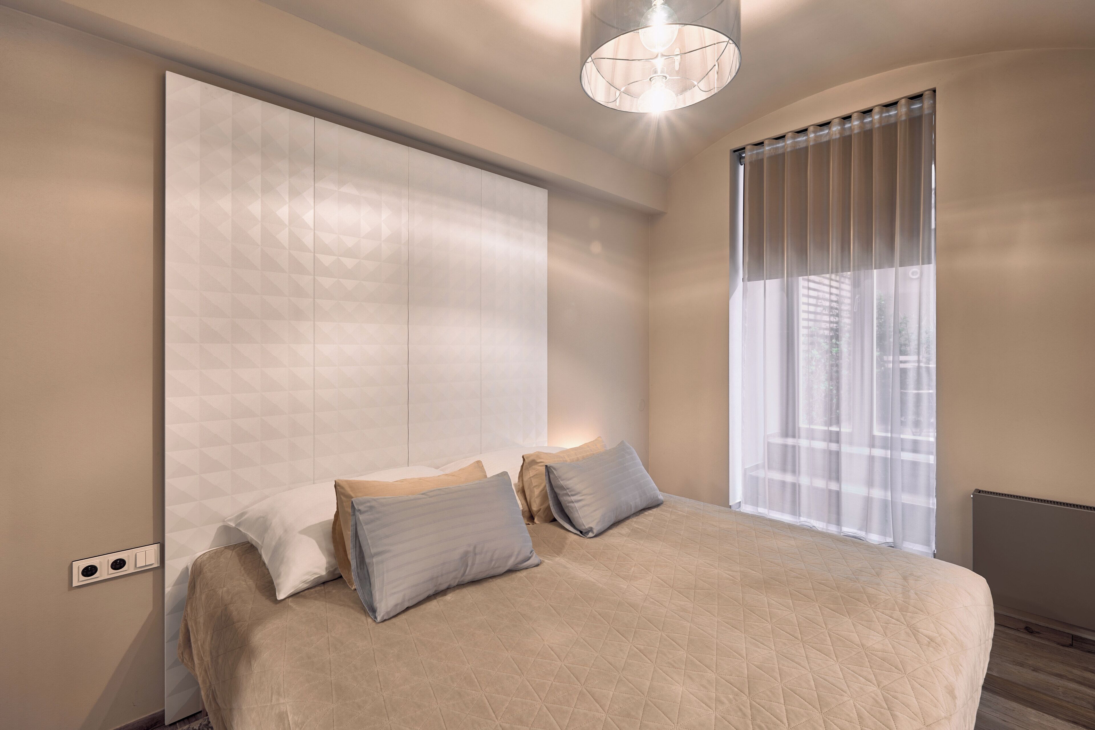 A bedroom with a large bed, a wardrobe, a window with sheer curtains, and a ceiling light fixture.