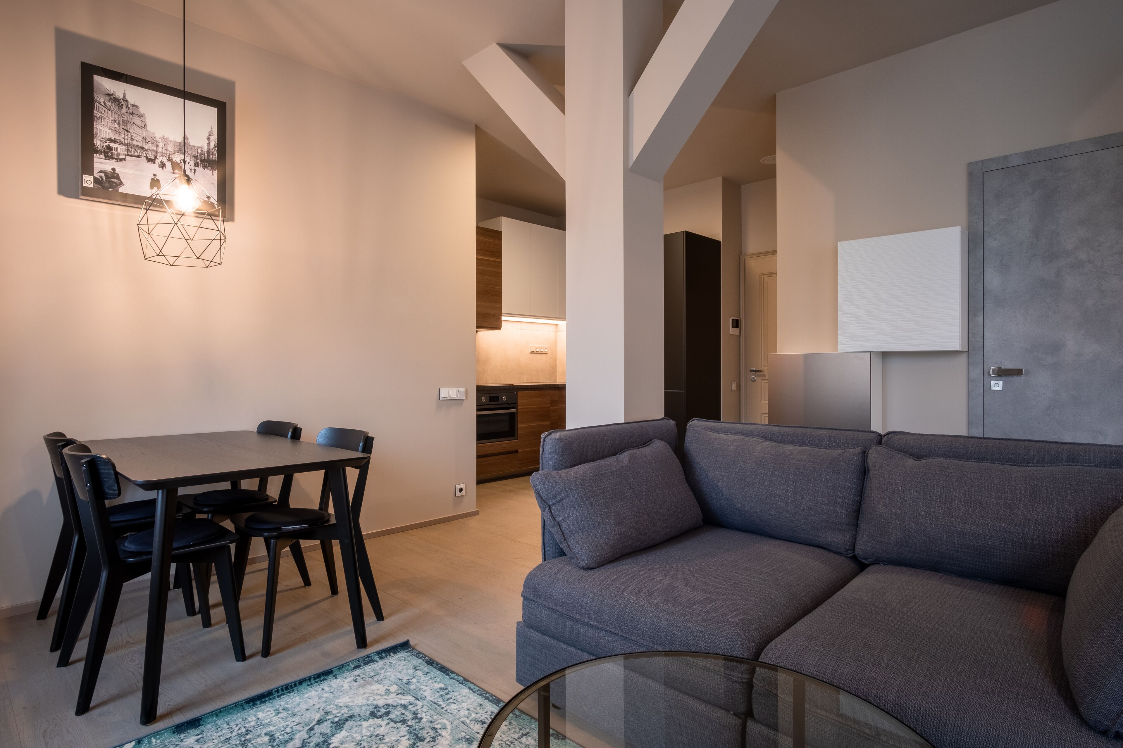 A modern living room with a gray sofa, a dining table with chairs, and a hanging light fixture.
