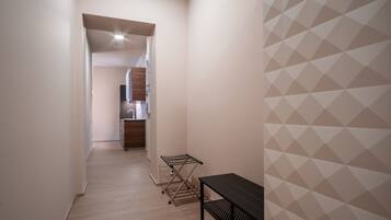 A narrow hallway with a wooden floor, a black metal drying rack, and a black metal shelf unit.