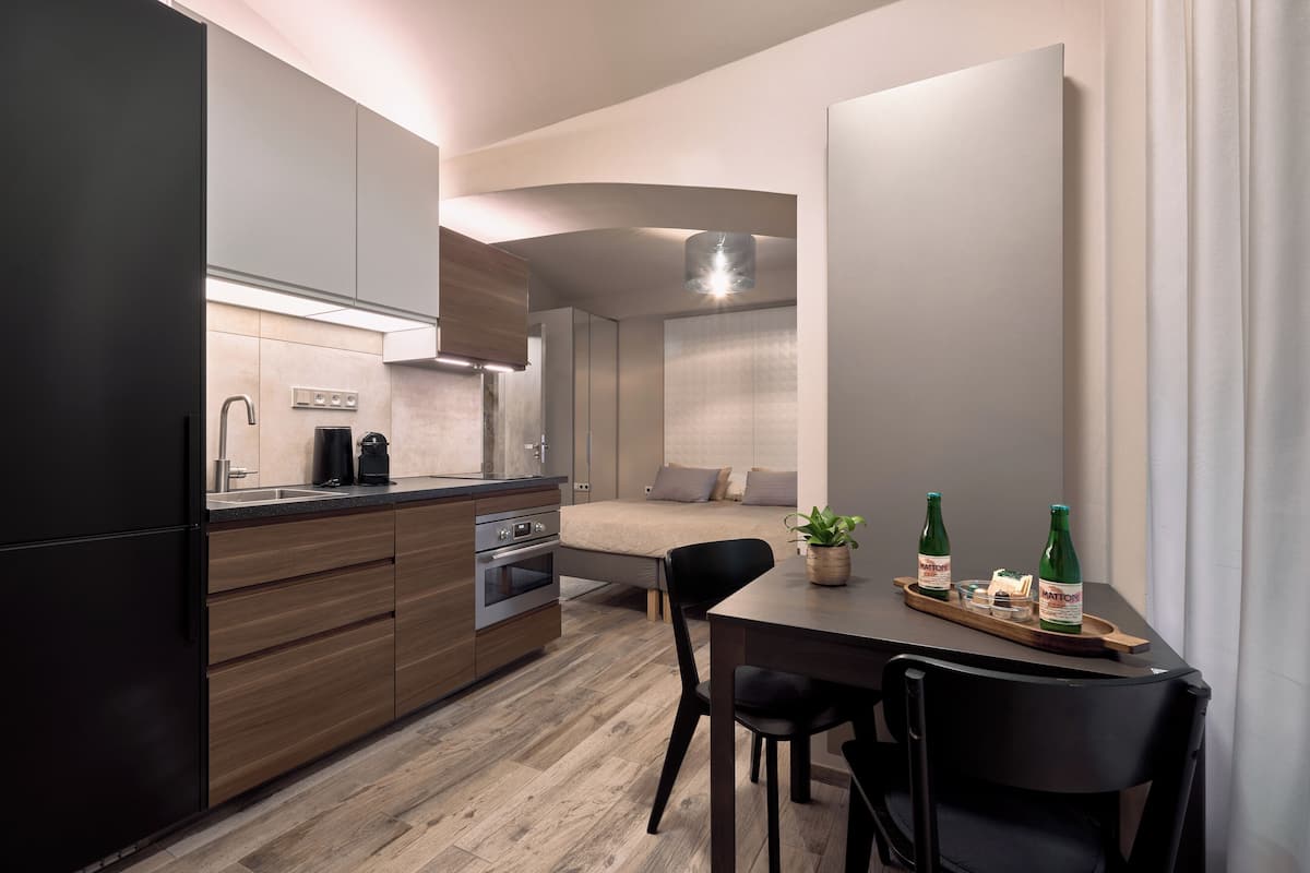 A compact kitchen with modern appliances, a dining area with a table and chairs, and a bed in the background.