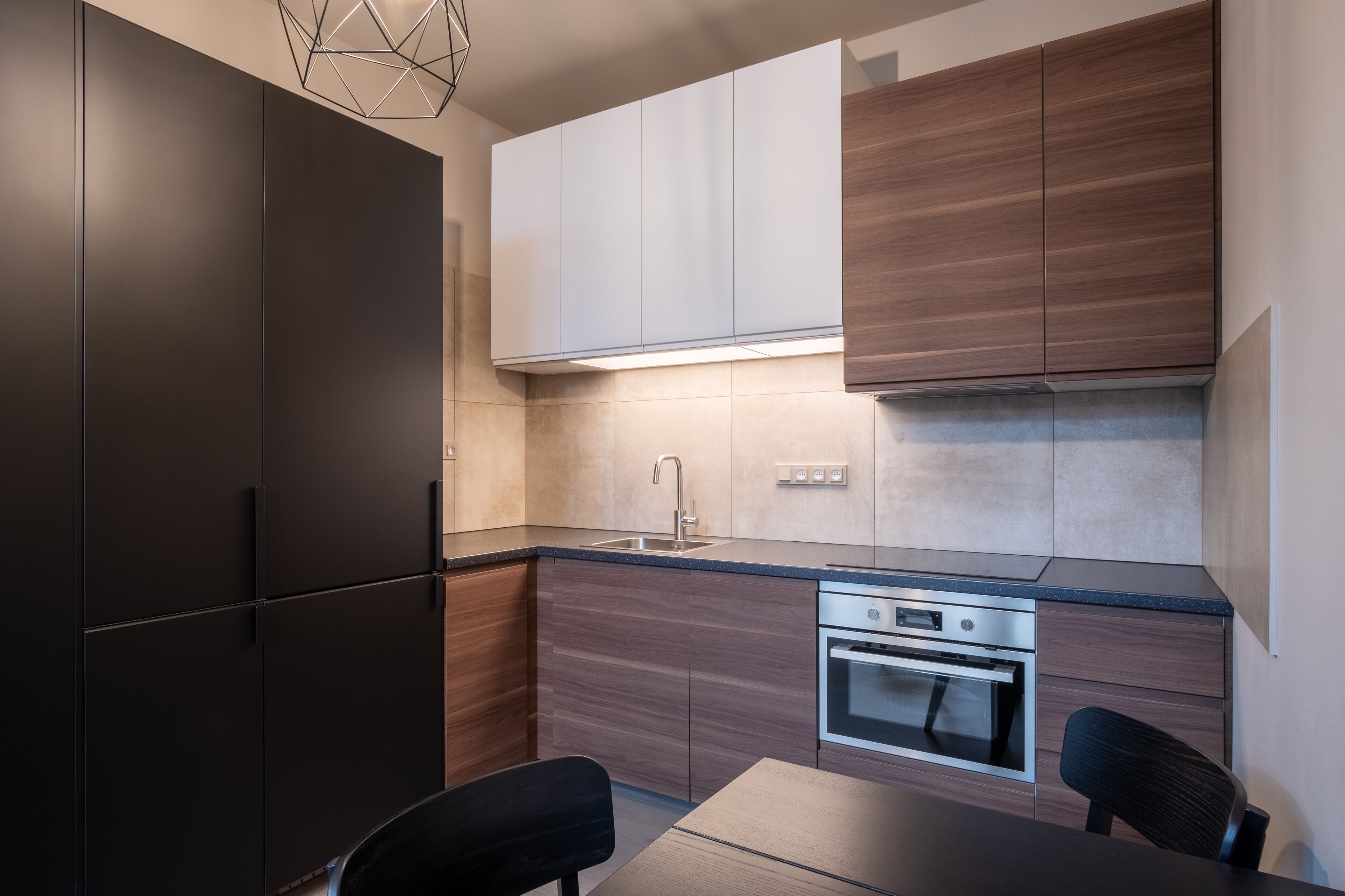 A modern kitchen with dark cabinets, a stainless steel oven, and a black dining table.