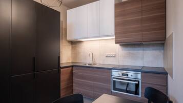 A modern kitchen with dark cabinets, a stainless steel oven, and a black dining table.