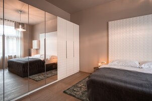 Quarto moderno com um espelho grande, duas camas, uma mesinha de cabeceira e um candeeiro suspenso.