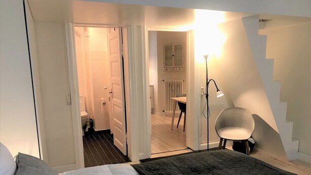 A bedroom with a bed, a chair, a staircase, and a bathroom visible through an open door. - Small Cozy Apartment in Frederiksberg (Frederiksberg)