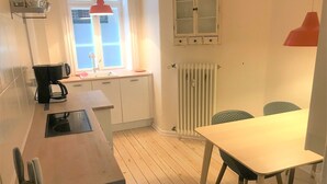 A small kitchen with a coffee maker, a sink, and a window. There is a table with chairs and a radiator below the window. - Small Cozy Apartment in Frederiksberg (Frederiksberg)