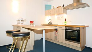 A compact kitchen with a wooden countertop, two bar stools, a built-in oven, and a stainless steel range hood. - Studio Apartment With Terrace, own Parking Space and a Small Lake 500 m Away (Papendorf)