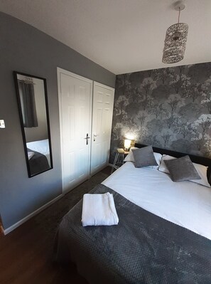 A bedroom with a bed, a mirror, a wardrobe, and a wall with a tree pattern. - Hardwick Haven, Sedgefield - Near Hardwick Hall (Stockton-on-Tees)