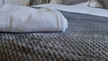 A bed with a textured grey blanket, a white towel, and a patterned wall in the background.