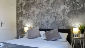 A bedroom with a bed, two bedside lamps, a door, and a wall with a tree pattern.
