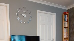 A living room with a television on a wooden stand, a bookshelf, and a wall clock.