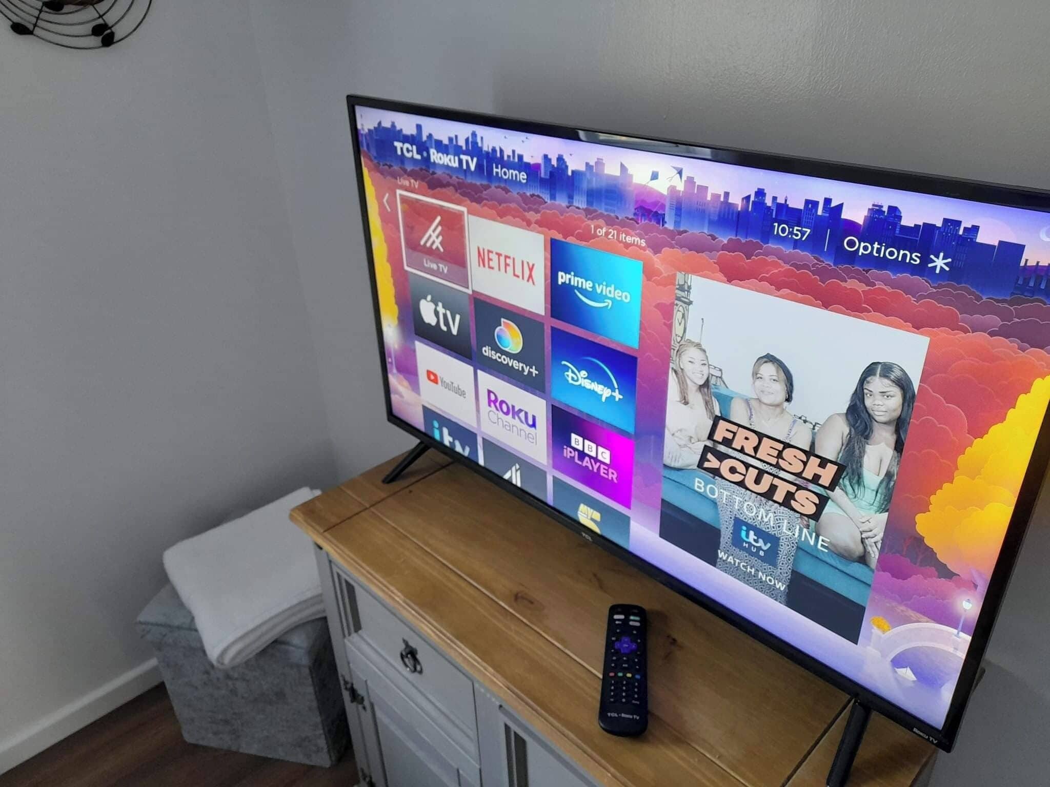 Un televisor mostrando una interfaz de servicio de streaming con varios logotipos, un control remoto y un cartel en la pared.