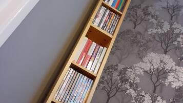 A bookshelf filled with books and DVDs against a wall with a tree pattern carpet.