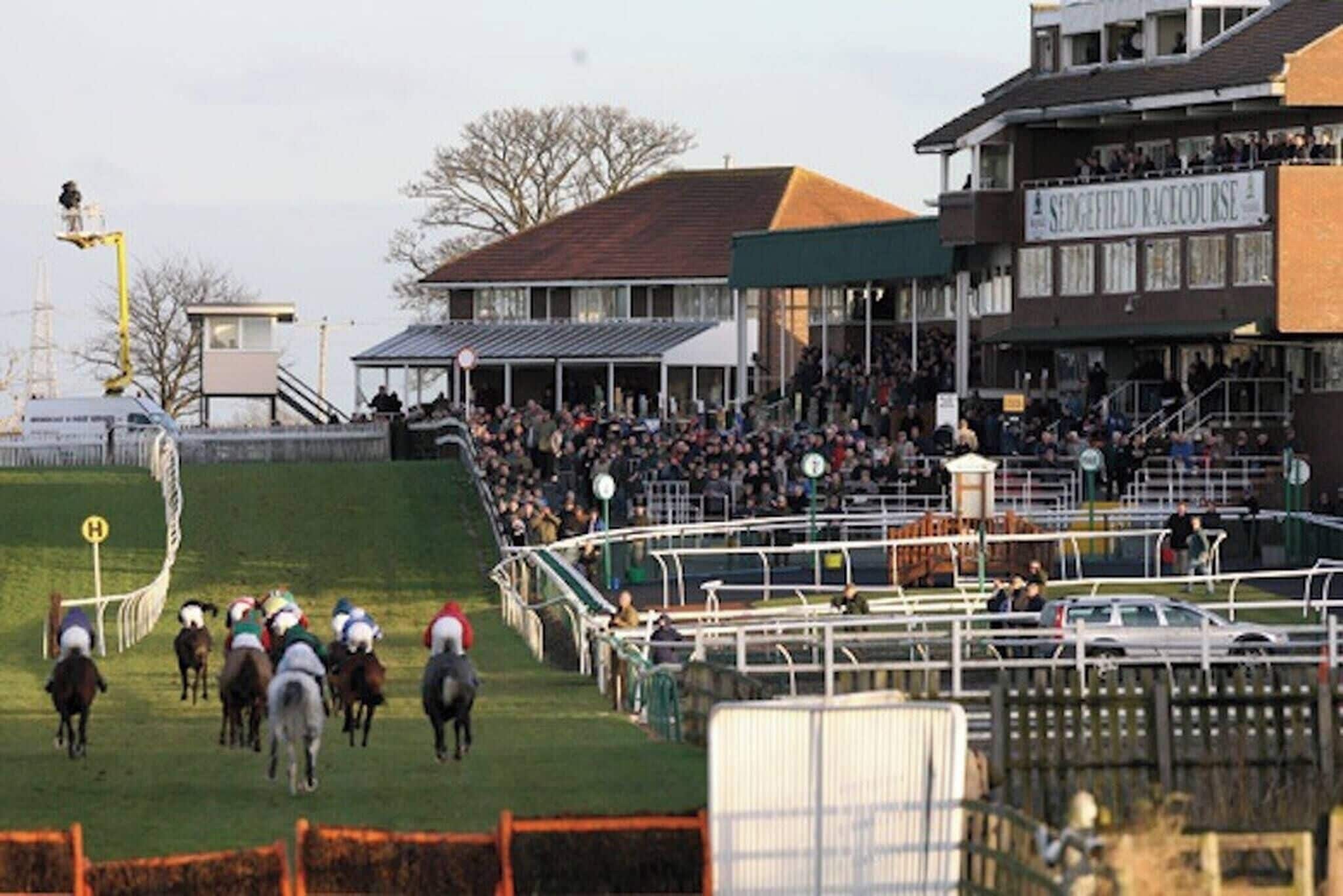 Un hippodrome avec des tribunes abritées, une foule de spectateurs et une piste délimitée par des clôtures.