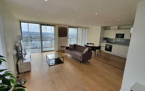 Enjoy city views from the large window in this open-plan living space featuring a sofa, dining area, and modern kitchen.