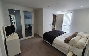 Relax in a serene bedroom with a large bed, flat-screen TV, and sliding door to a bathroom with a shower.