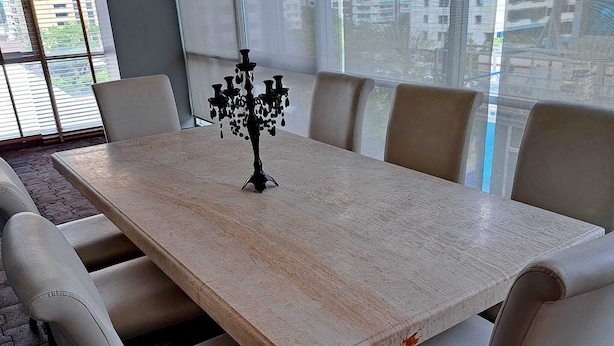 Een rechthoekige eettafel met een donker, versierd middelpunt, omringd door zes beiges fauteuils.