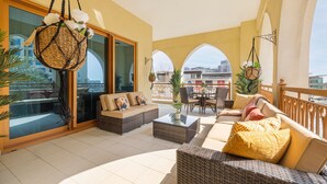 A spacious balcony with wicker furniture, a glass door leading to a terrace, and a view of the cityscape. - Large Terrace and Pool View - 2 Br - Next to Mall (Dubai)